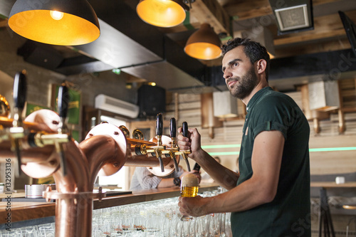 Bartender in coffee shop pouring beer from tap photo