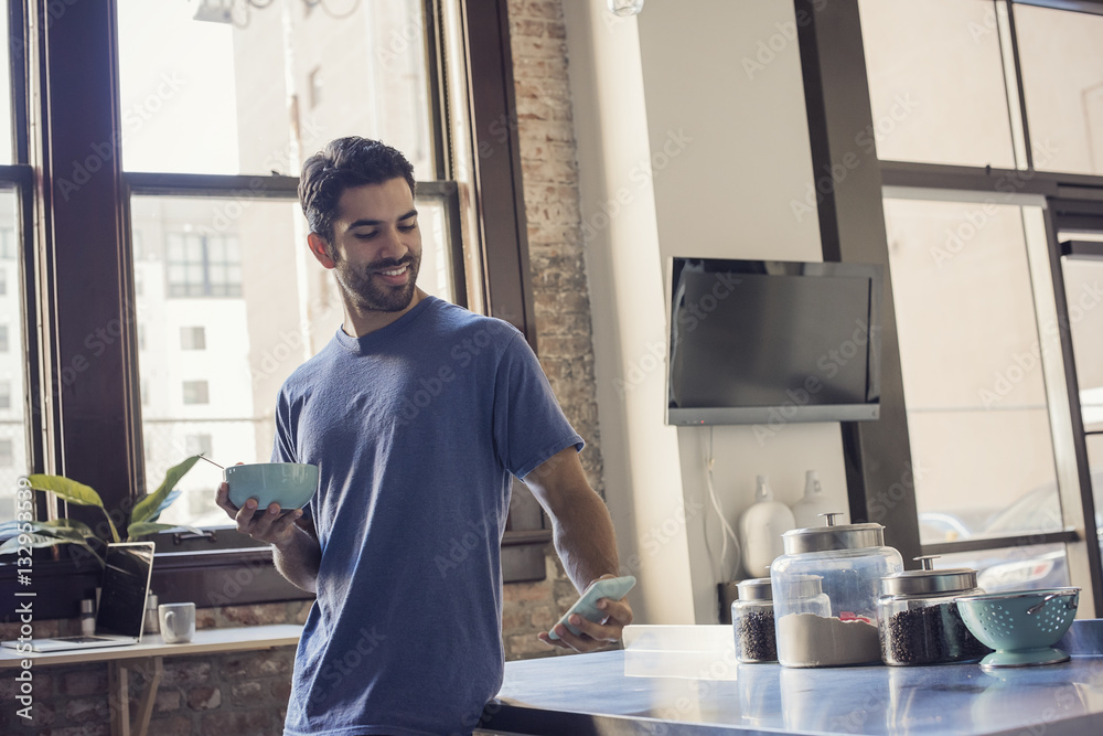 Young man standing in kitchen using smart phone Young man standing in kitchen using smart phone
