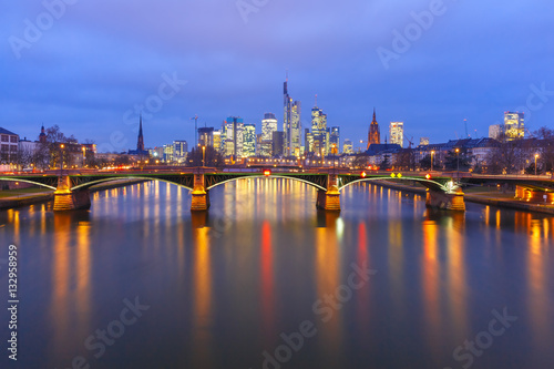 Picturesque view of Frankfurt am Main skyline and Ignatz Bubis Brucke bridge during evening blue hour with mirror reflections in the river, Germany