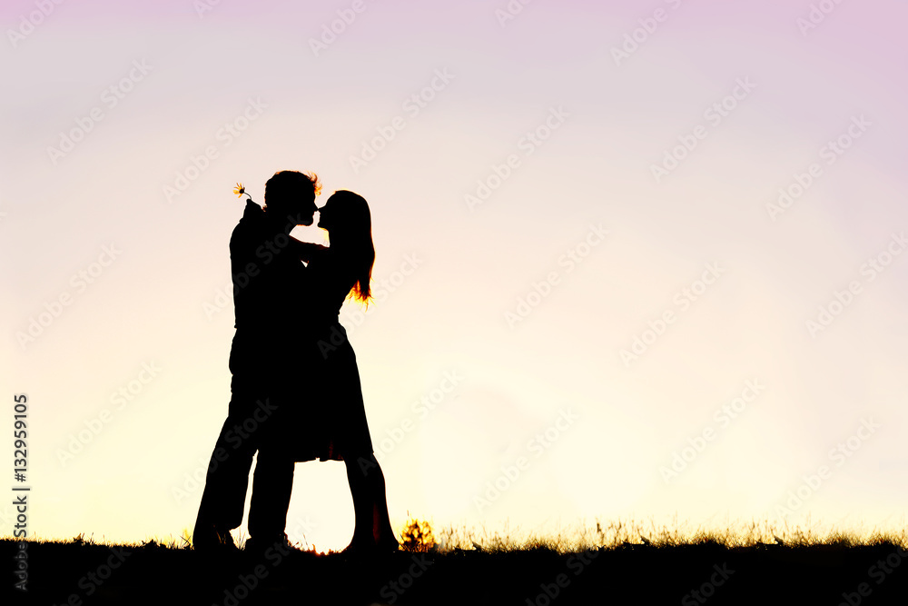 Silhouette of Loving Young Couple Hugging at Sunset Outside