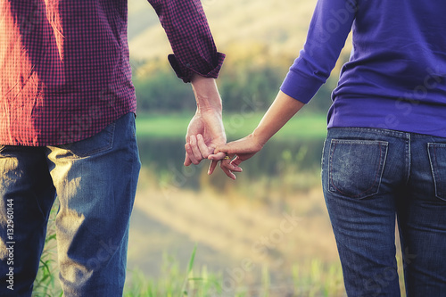 Happy couple holding hands, looking into the landscape and watching sunset while the summer vacations..