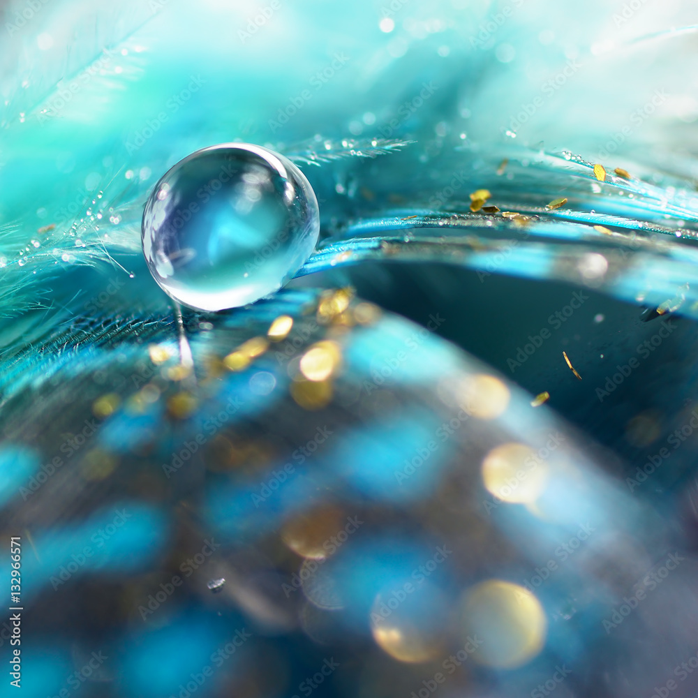 Big blue dew drop of rain water on a blue bird feather and gold tinsel  close-