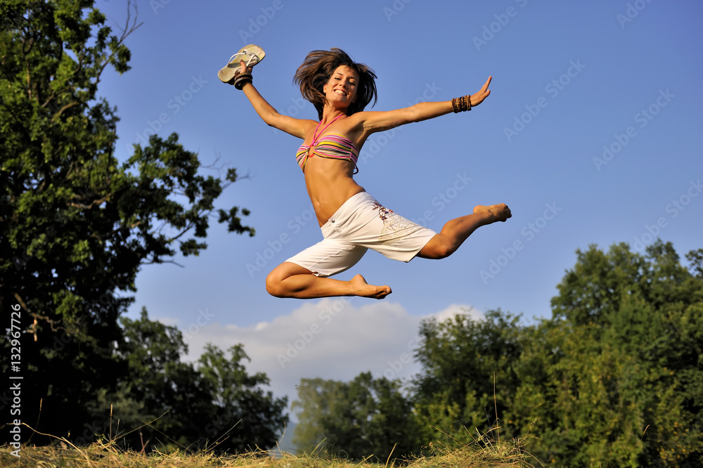 Happy woman jumping on summer time. She is wearing short white pants and  bikini. She is holding flip-flops in her hand. she was jumping on trampoline  Stock Photo | Adobe Stock