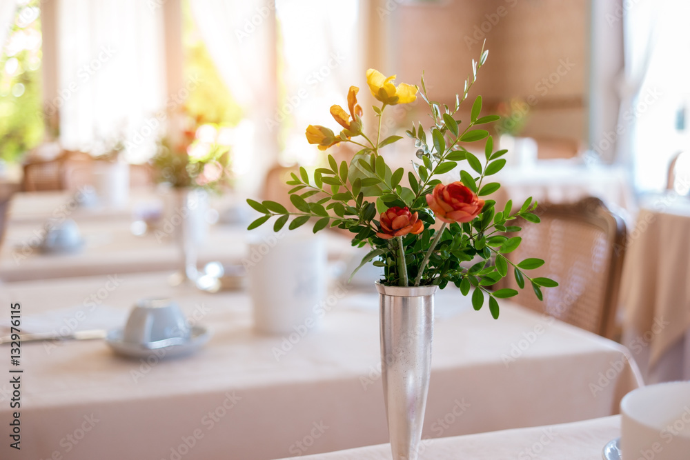Vase with flowers and leaves. Blurred dining tables. Tasty food and calm atmosphere.
