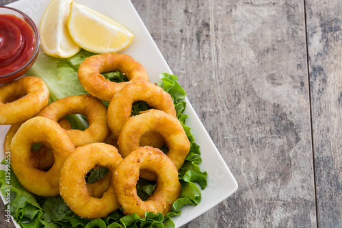 Fried calamari rings with lettuce and ketchup on wooden background
