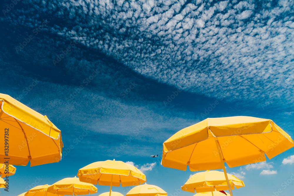 Fototapeta premium Several yellow umbrellas on the beach against blue sky with clou