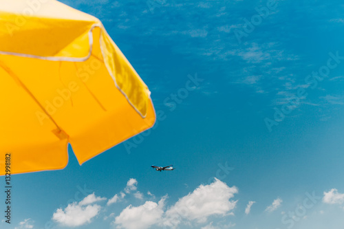 Yellow umbrella on the beach against blue sky with clouds and pl