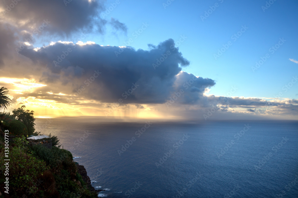 sunset on the sea coast. The ocean, vegetation, clouds, illuminated by the sun and the rain