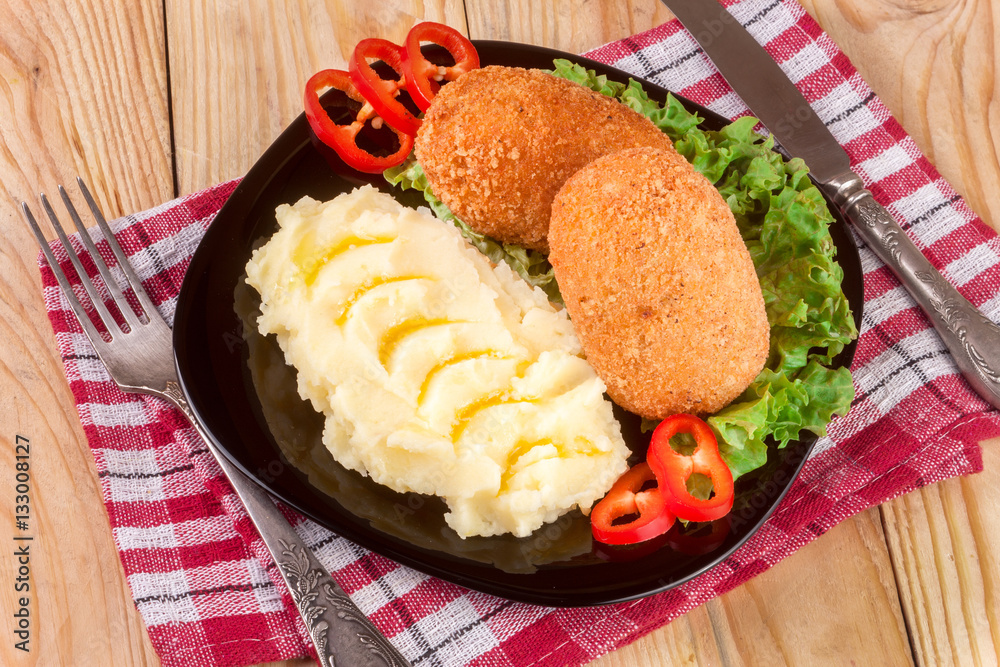 two fried breaded cutlet with mashed potatoes and lettuce on a black plate wooden background