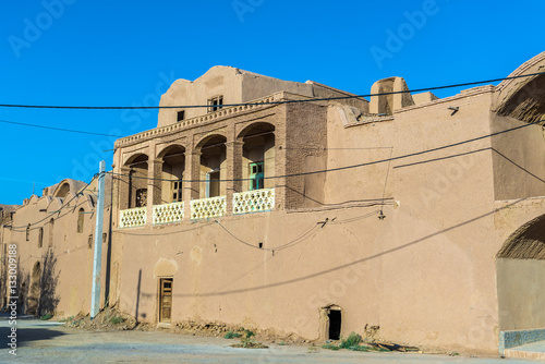 Building with entry gate to odl part, abandoned mud brick village of Kharanaq in Iran photo