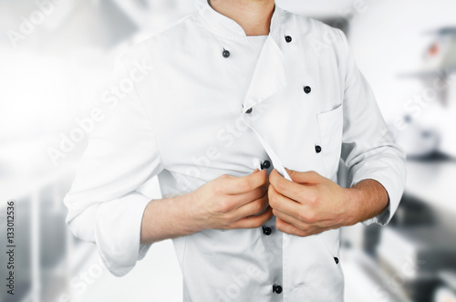 Chef buttoning his uniform on the kitchen background.