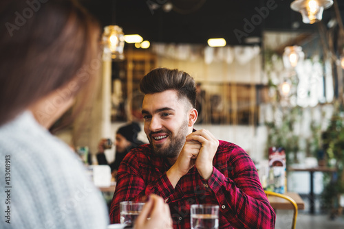 Photos Young hipster man sitting in the cafeteria, smiling and listening his girlfriend