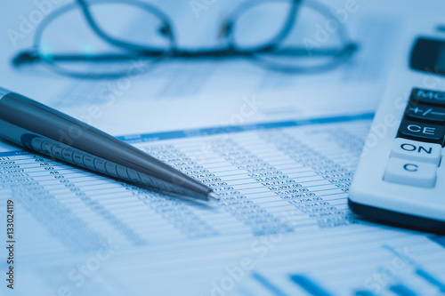 Finance, financial analysis, accounting accounts spreadsheet with pen glasses and calculator in blue. Close up concept for stock, bank accounting and book keeping data. 
