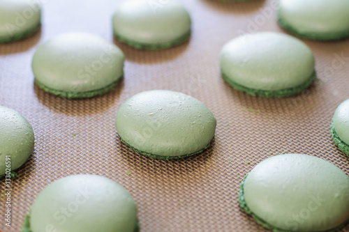 Green macaron shells arranged on a baking mat