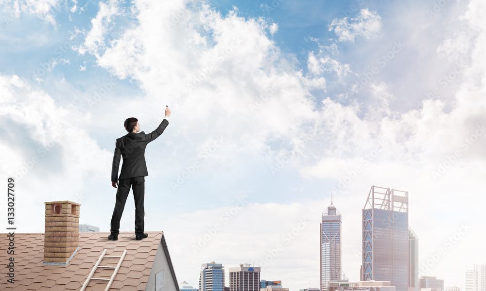 Businessman on house roof touch empty space. Mixed media Businessman on house roof touch empty space. Mixed media