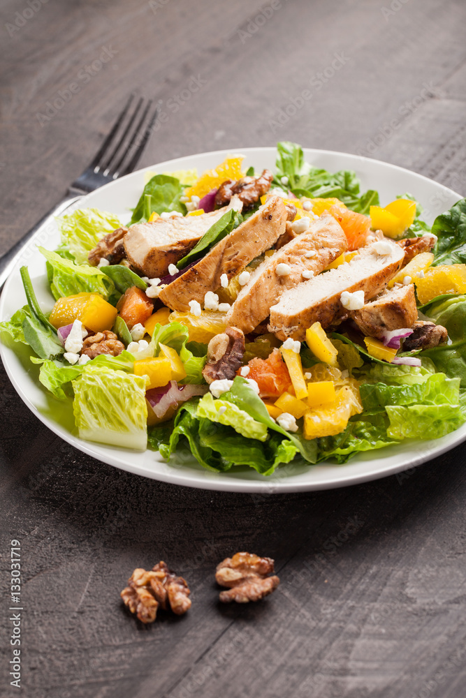 Orange Walnut Chicken Salad  on a white plate with  dark wooden background topped with orange vinaigrette dressing