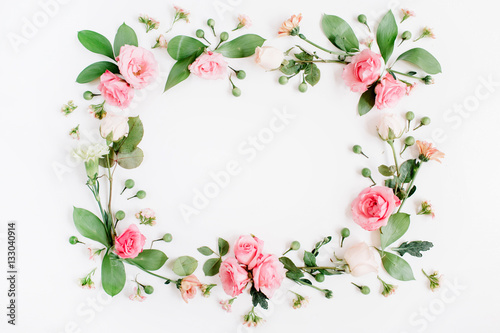 Round frame made of pink and beige roses, green leaves, branches on white background. Flat lay, top view. Valentine's background