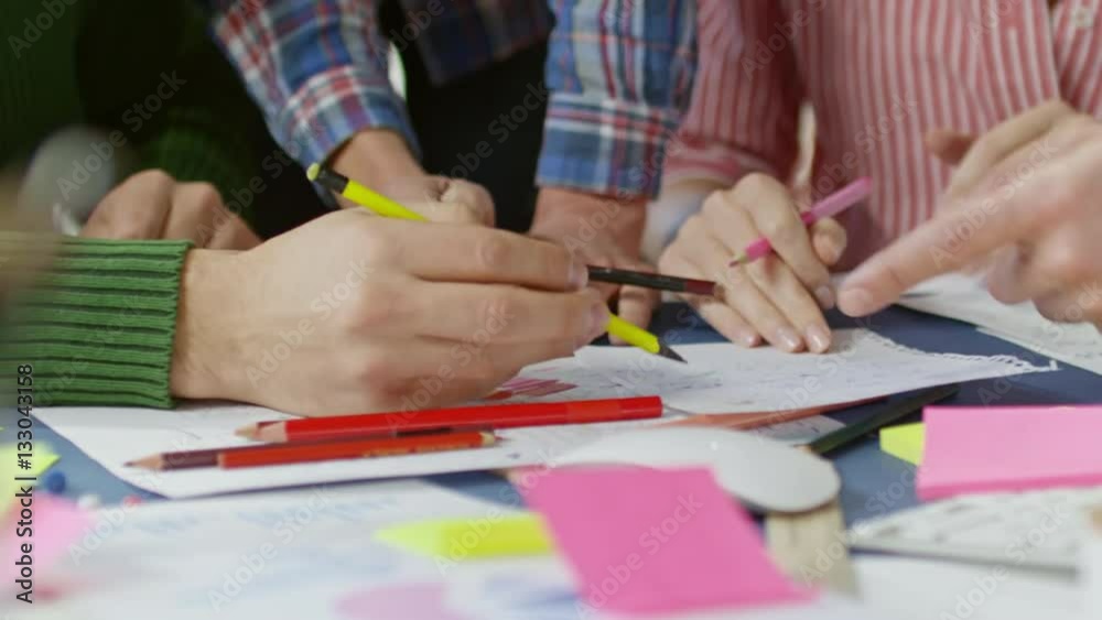 PAN with mid-section of hands of designers with coloring pencils discussing draft for new project PAN with mid-section of hands of designers with coloring pencils discussing draft for new project