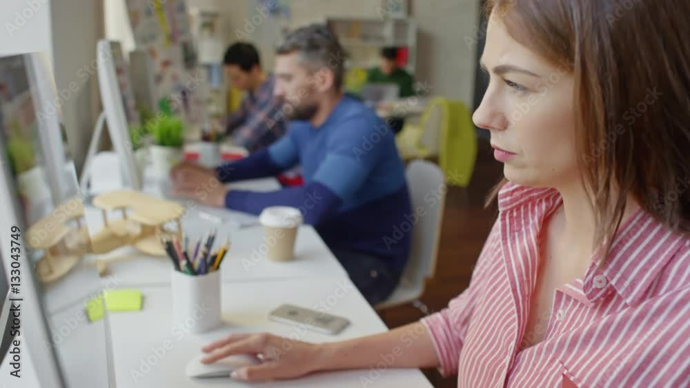 Tilt down of attractive businesswoman sitting in office and typing on computer with colleagues working beside her Tilt down of attractive businesswoman sitting in office and typing on computer with colleagues working beside her