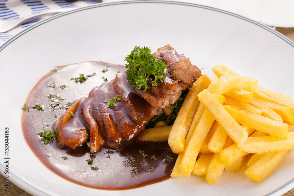 A nice dish of roasted duck breast confit in orange sauce served with fries on the table