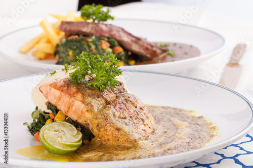 Fototapeta Naklejka Na Ścianę i Meble -  A decorating nice dish of salmon steak and beef served with mashed potato,lemon, saute spinach and sauce on background with wooden utensils.