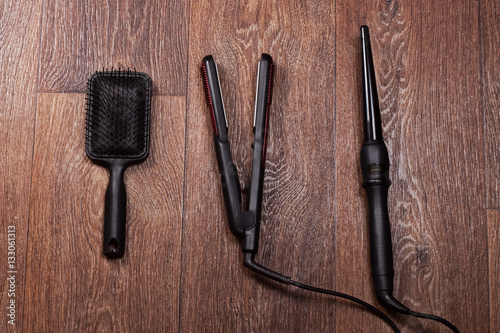 black square comb, hair iron and curling hair on wooden background