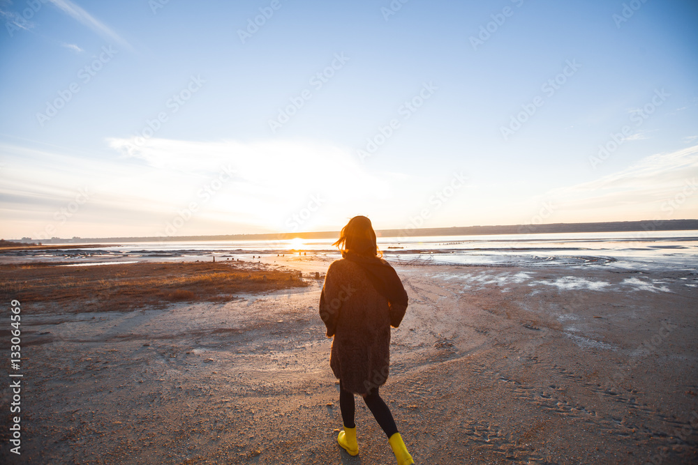 Beautiful girl is standing on the sea in a Sunbeam, yellow boots, long