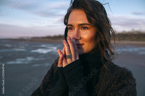 Beautiful girl is standing on the sea in a Sunbeam, yellow boots, long black coat, sand underfoot