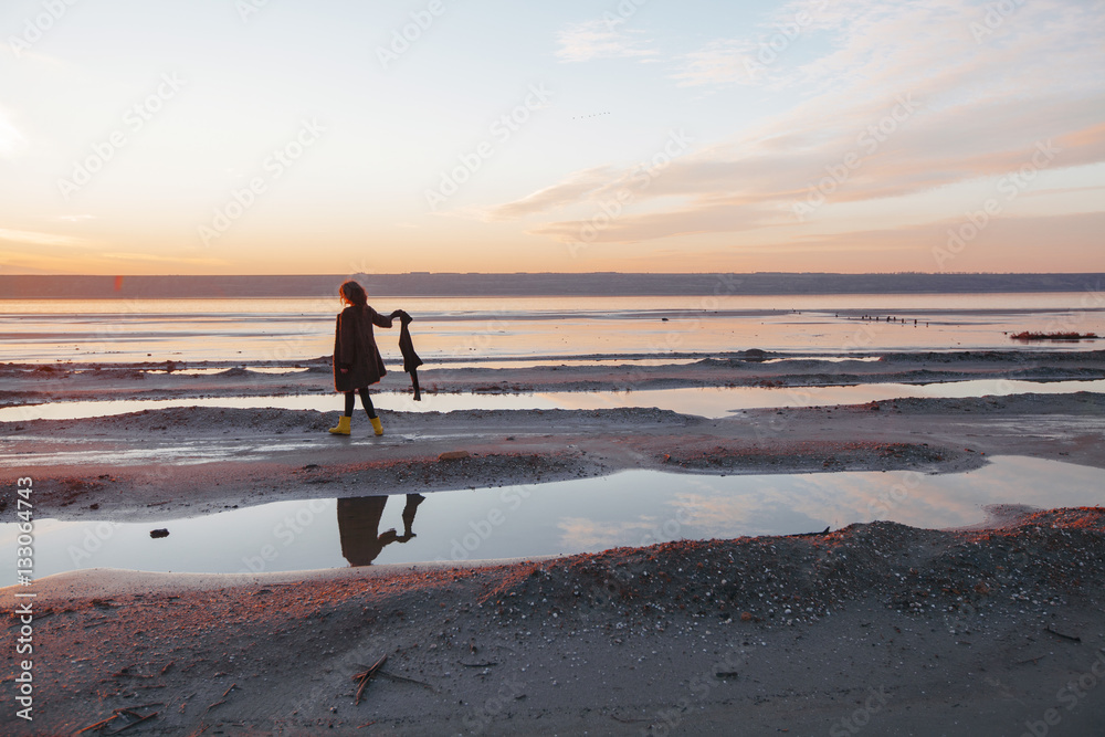 Beautiful girl is standing on the sea in a Sunbeam, yellow boots, long