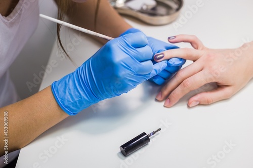 Professional beautician applying nail polish to female nail