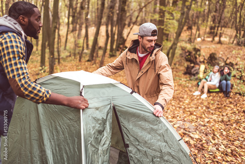 Slika na platnu Men pitching tent in autumn forest
