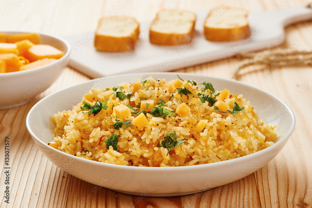Pumpkin risotto on white dish, slices of bread on chopping board in the background Pumpkin risotto on white dish, slices of bread on chopping board in the background