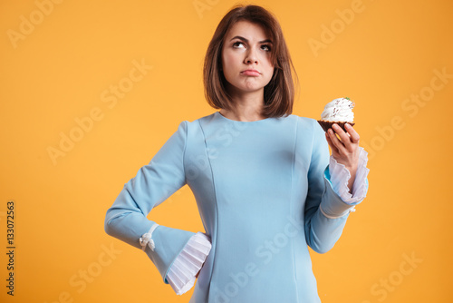 Thoughtful young woman holding cupcake and thinking