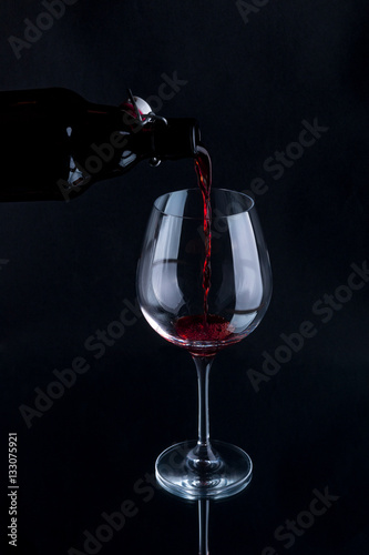 Red wine pouring into a wineglass. Isolated on black background.