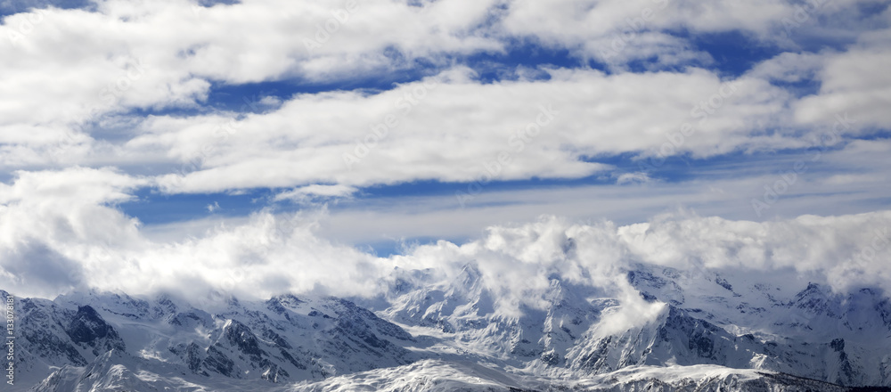 Panoramic view on snow mountains and sunlight cloudy sky at wint