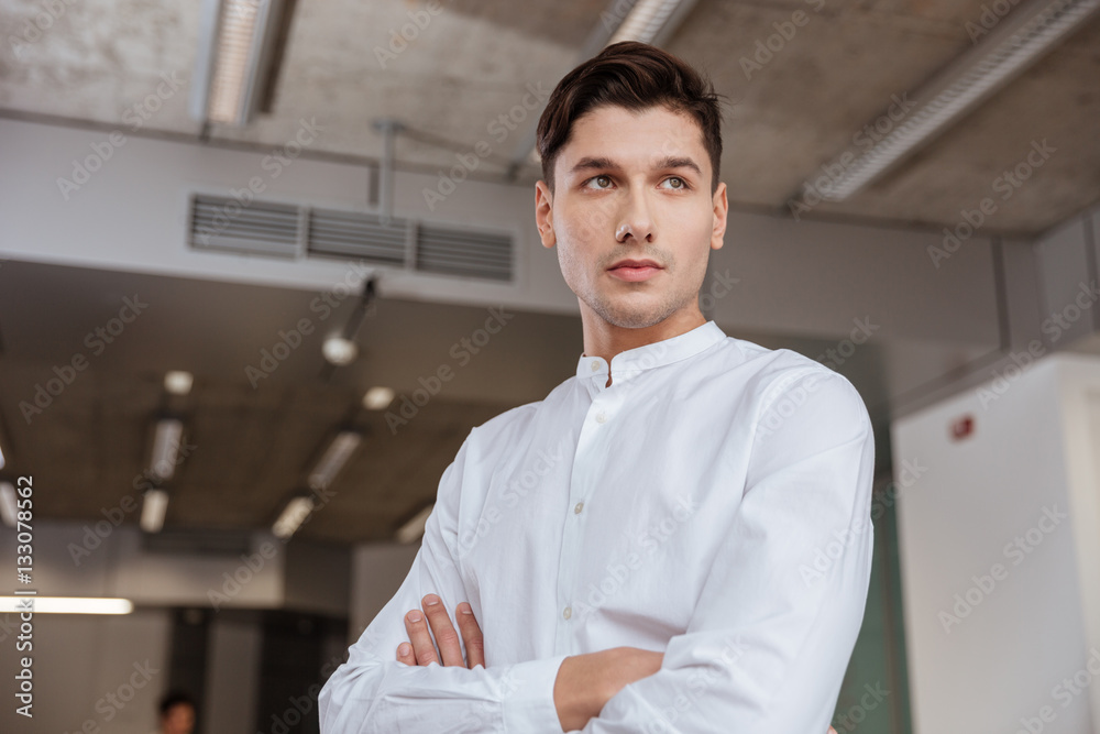 Serious man standing with arms crossed indoors