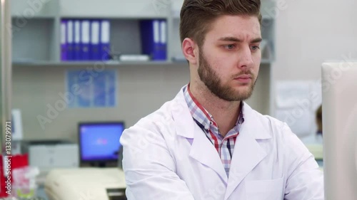 Wallpaper Mural Handsome caucasian man using computer at the laboratory. Young male scientist typing on keyboard at the lab. Close up of bearded guy in white coat doing his job Torontodigital.ca