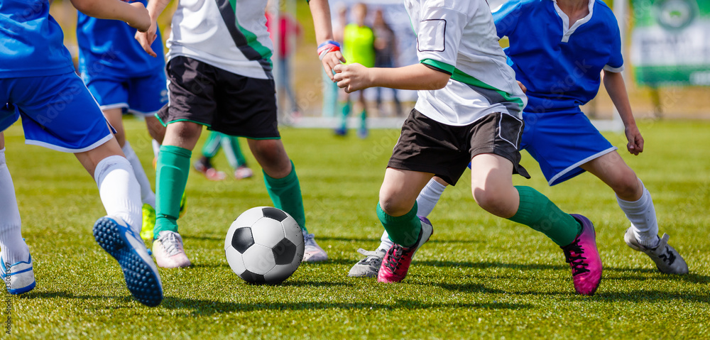 Young Boys Soccer Players Kicking Football on the Sports Field. Running Footballers in Blue and White Jerseys. Soccer Horizontal Background Young Boys Soccer Players Kicking Football on the Sports Field. Running Footballers in Blue and White Jerseys. Soccer Horizontal Background