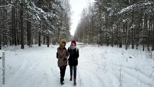Two young and attractive women walking along the forest's trail and talking about something