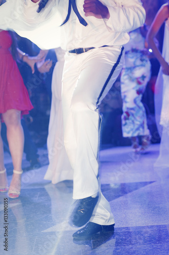 Dancer in white suit and lacquer shoes moves in blue lights
