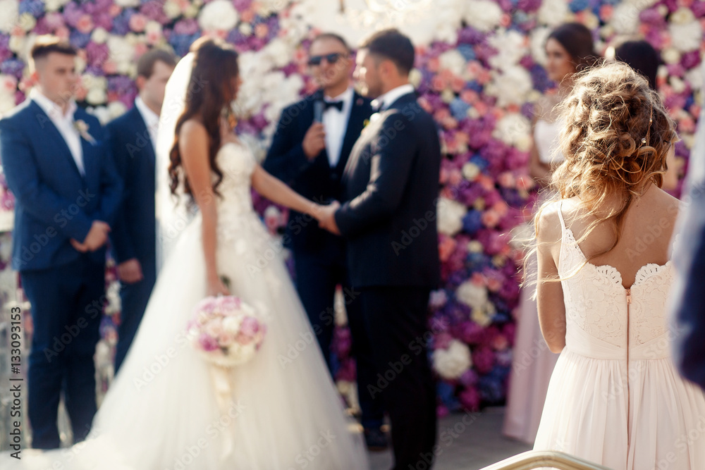 Tender lady with dark blonde hair looks at bride and groom stand