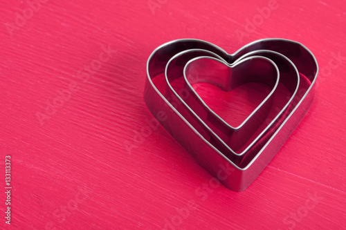 Valentine background with three metal hearts on pink wood.