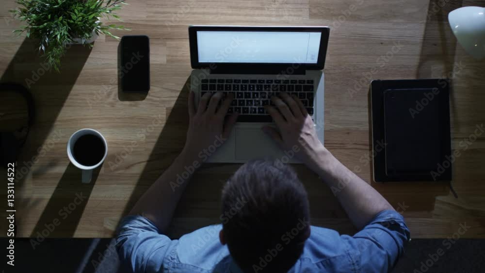Top View of Creative Designer Working on His Laptop at Night. His Table is Illuminated by Cold Blue Light From Outside. Shot on RED Cinema Camera in 4K (UHD). Top View of Creative Designer Working on His Laptop at Night. His Table is Illuminated by Cold Blue Light From Outside. Shot on RED Cinema Camera in 4K (UHD).