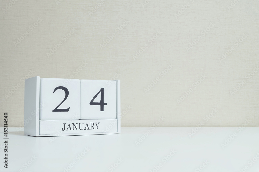 Closeup white wooden calendar with black 24 january word on blurred white wood desk and cream color wallpaper in room textured background with copy space , selective focus at the calendar
