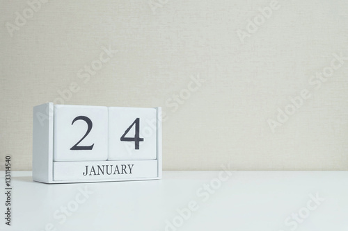 Closeup white wooden calendar with black 24 january word on blurred white wood desk and cream color wallpaper in room textured background with copy space , selective focus at the calendar