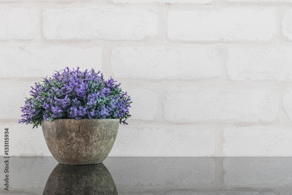 Fototapeta premium Closeup artificial purple plant on pot for decorate on black glass table and white brick wall textured background with copy space