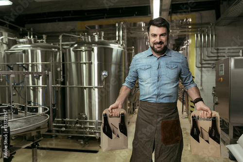 Happy man holding bottles of alcohol in brewery