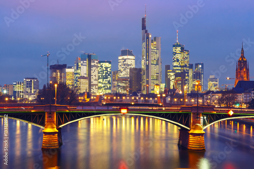 Fototapeta Naklejka Na Ścianę i Meble -  Picturesque view of Frankfurt am Main skyline and Ignatz Bubis Brucke bridge during evening blue hour with mirror reflections in the river, Germany