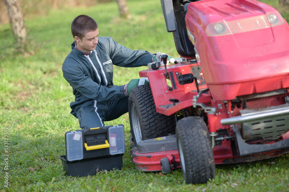 Naklejka premium Young man repairing ride on mower