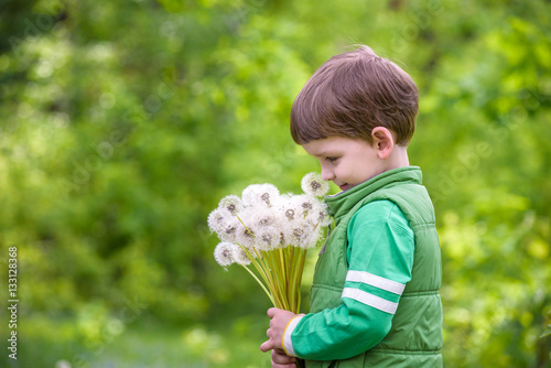 Cute 4 years old boy with dandelion outdoors at sunny summer day.